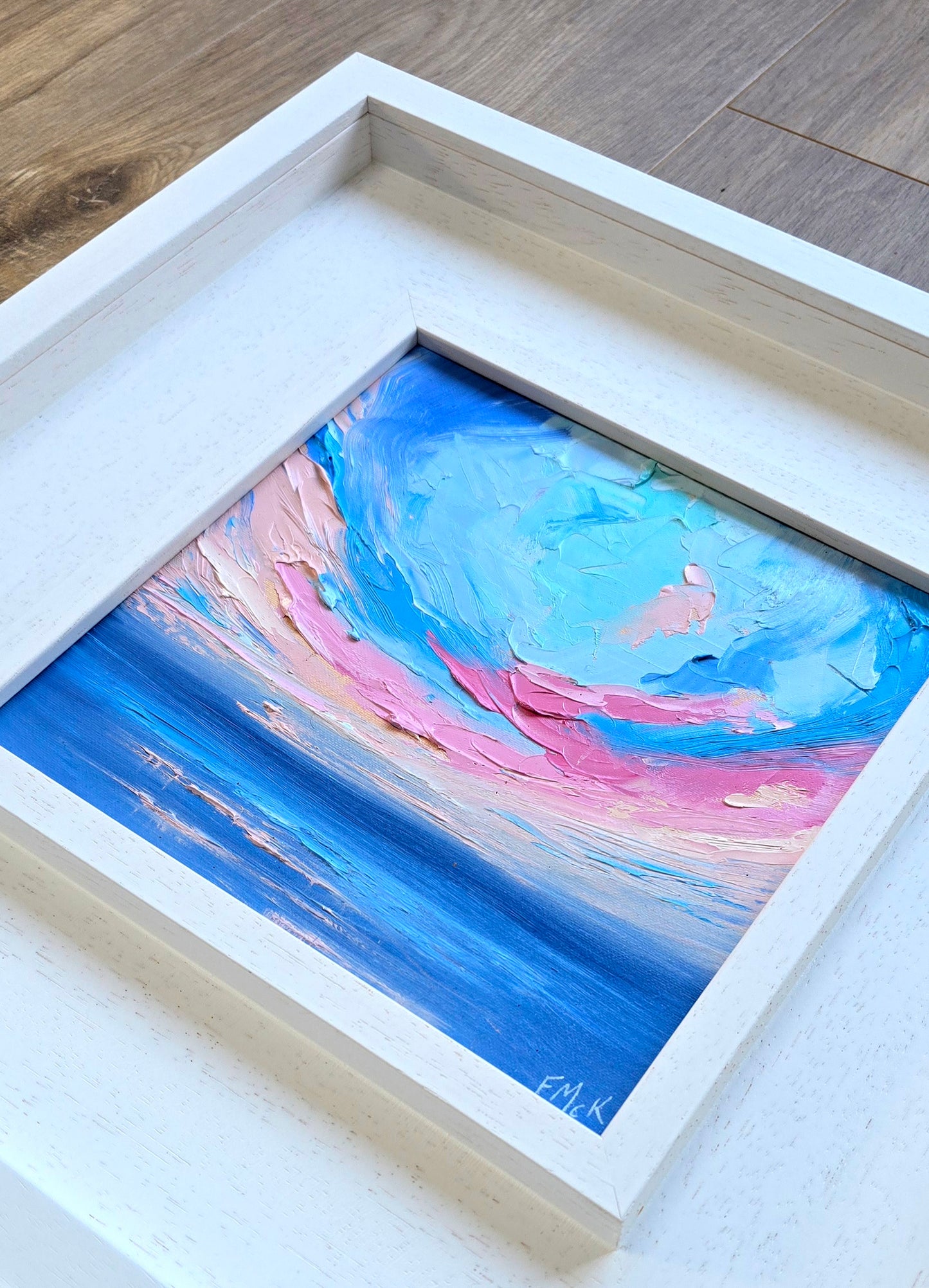Framed abstract coastal painting with blue and pink hues