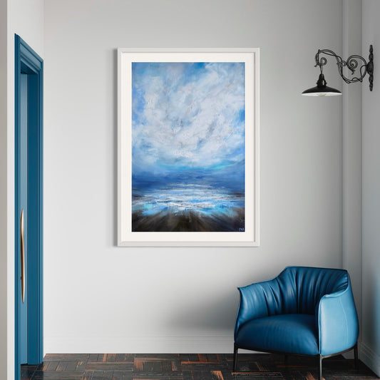 A painting titled 'Serenity' depicting a calm seascape with a cloud-filled sky, displayed on a wall above a blue chair, with a white frame around the painting.