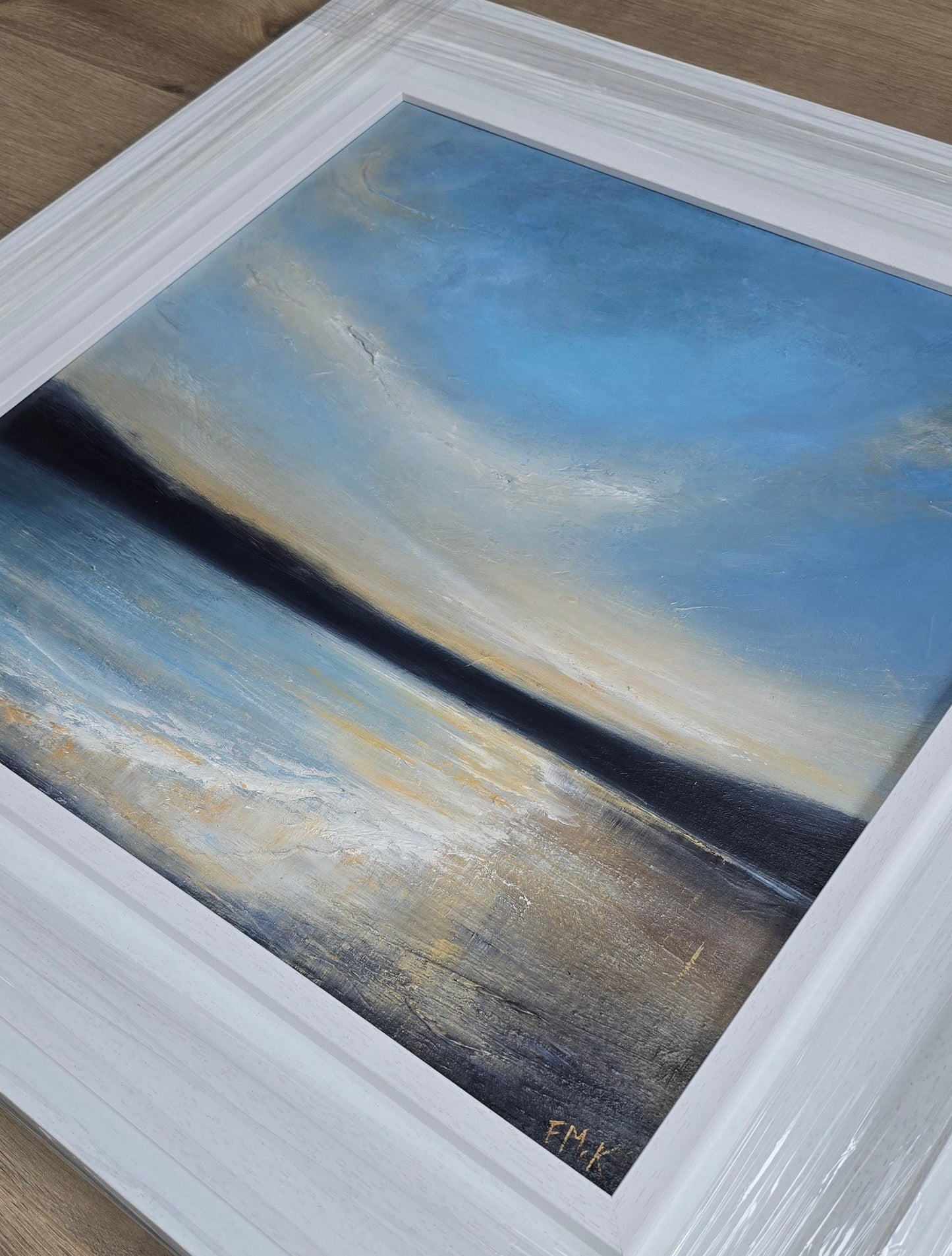 Framed abstract painting with blue and beige tones on a wooden surface