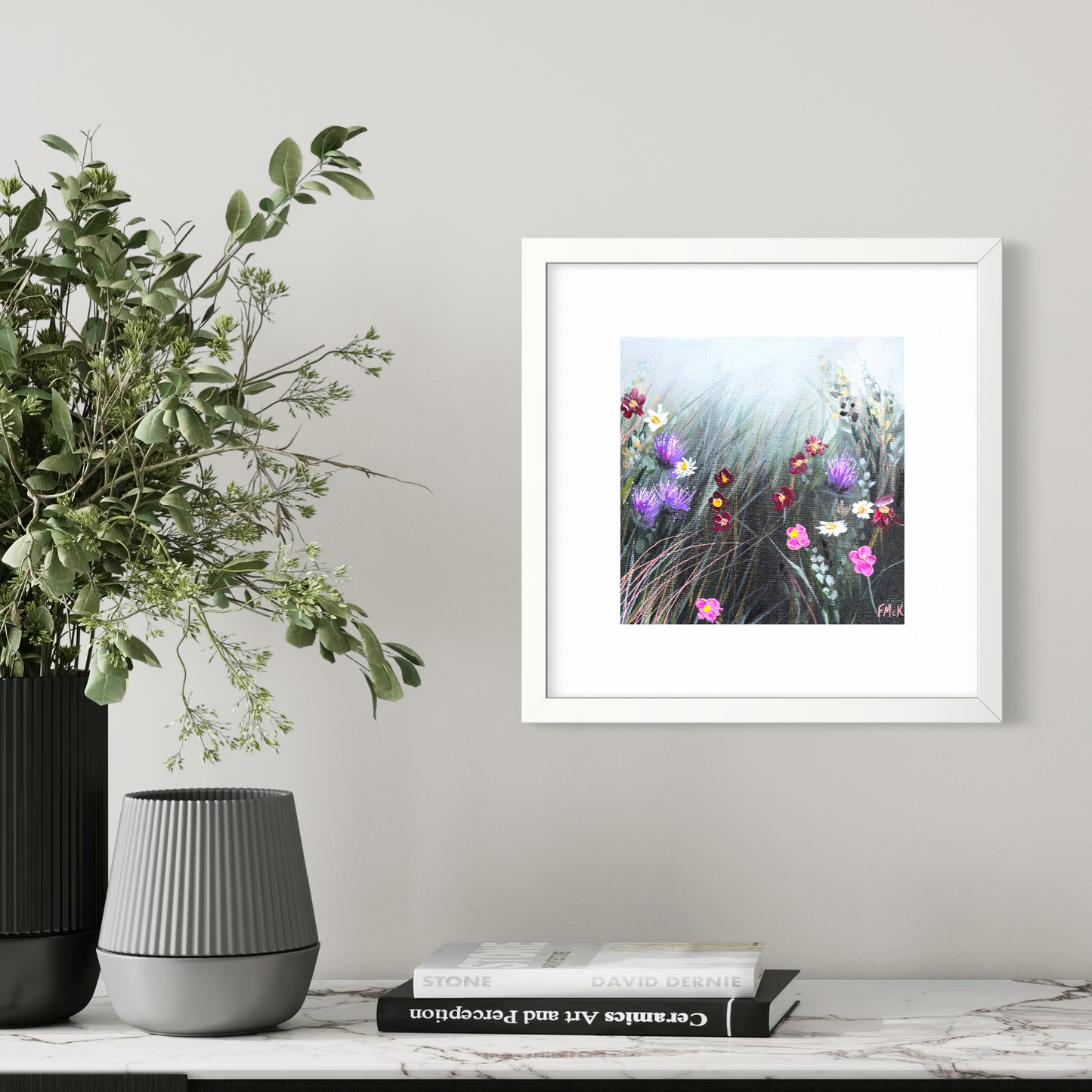 Framed artwork of flowers on a wall next to a plant and books.