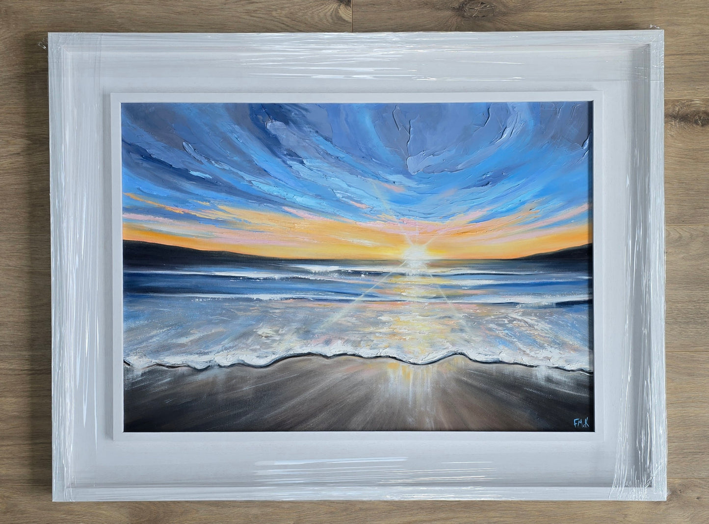 Framed painting of a sunset over water with a white frame.