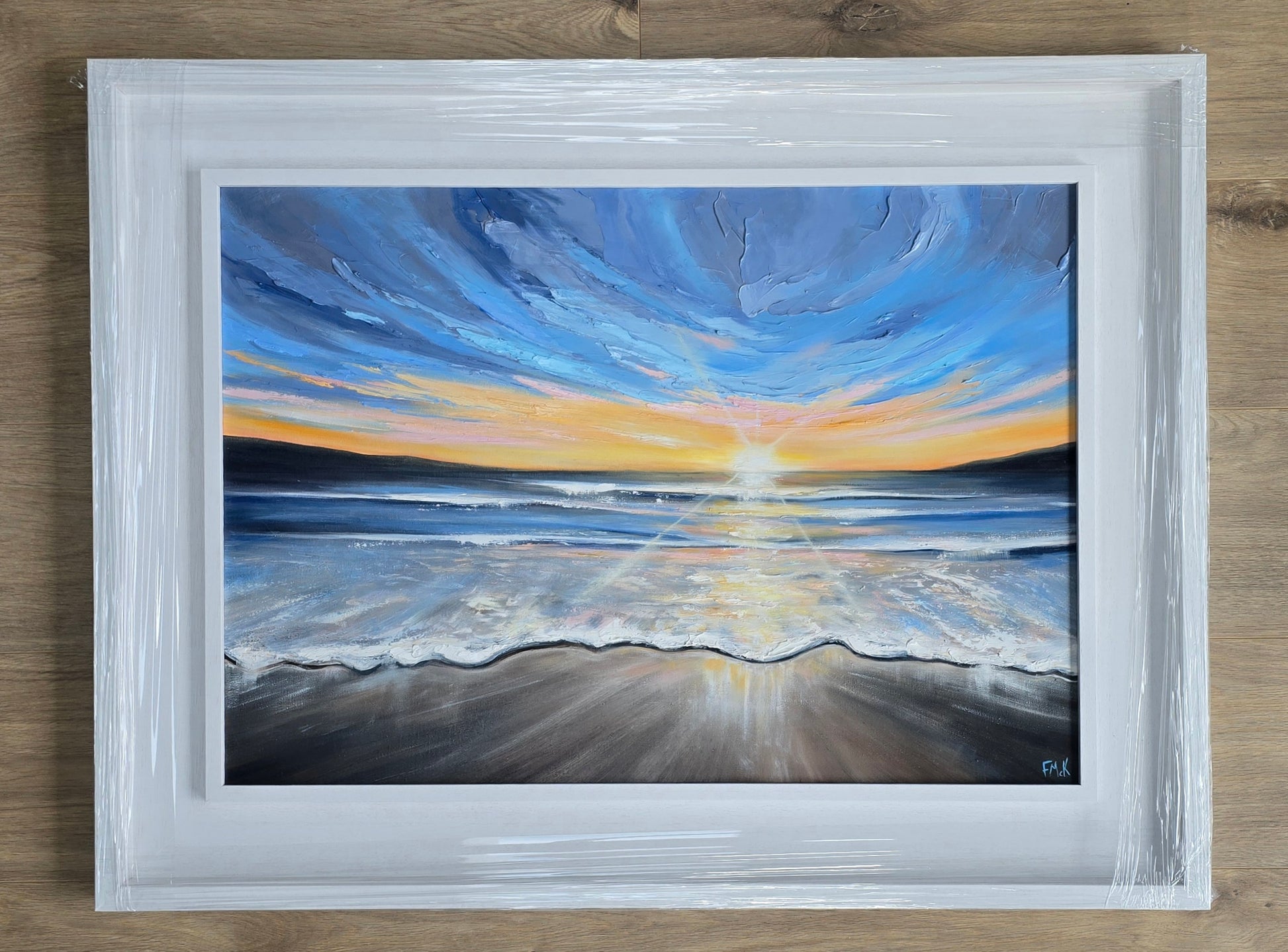 Framed painting of a sunset over water with a white frame.