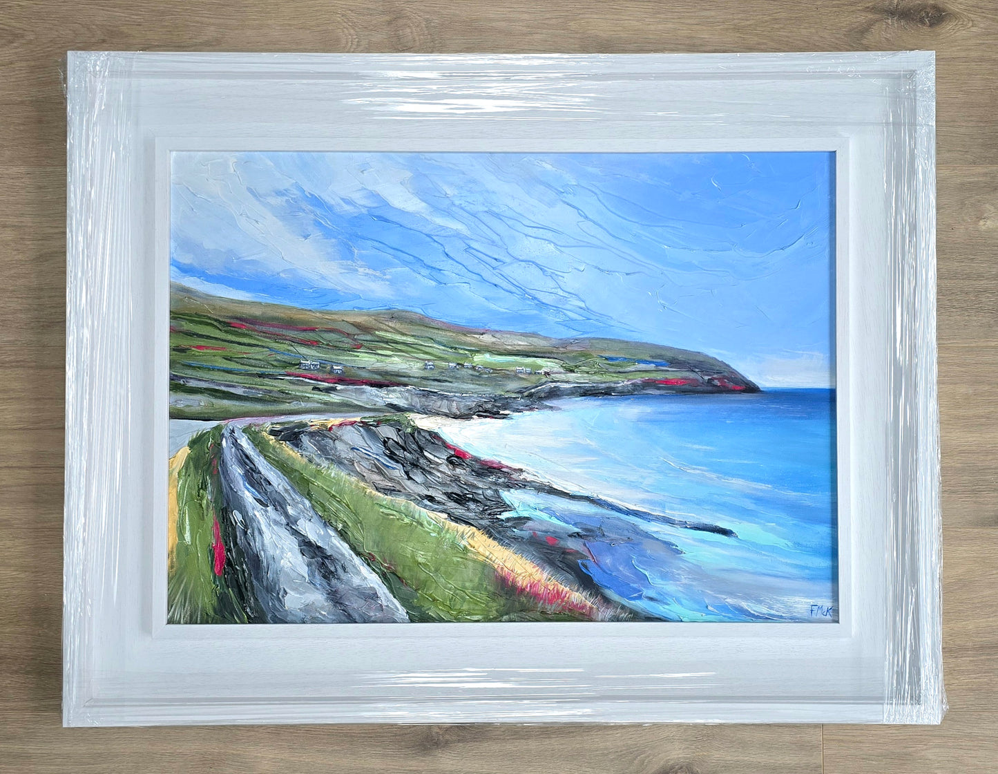 Framed painting of a coastal landscape with a white frame.