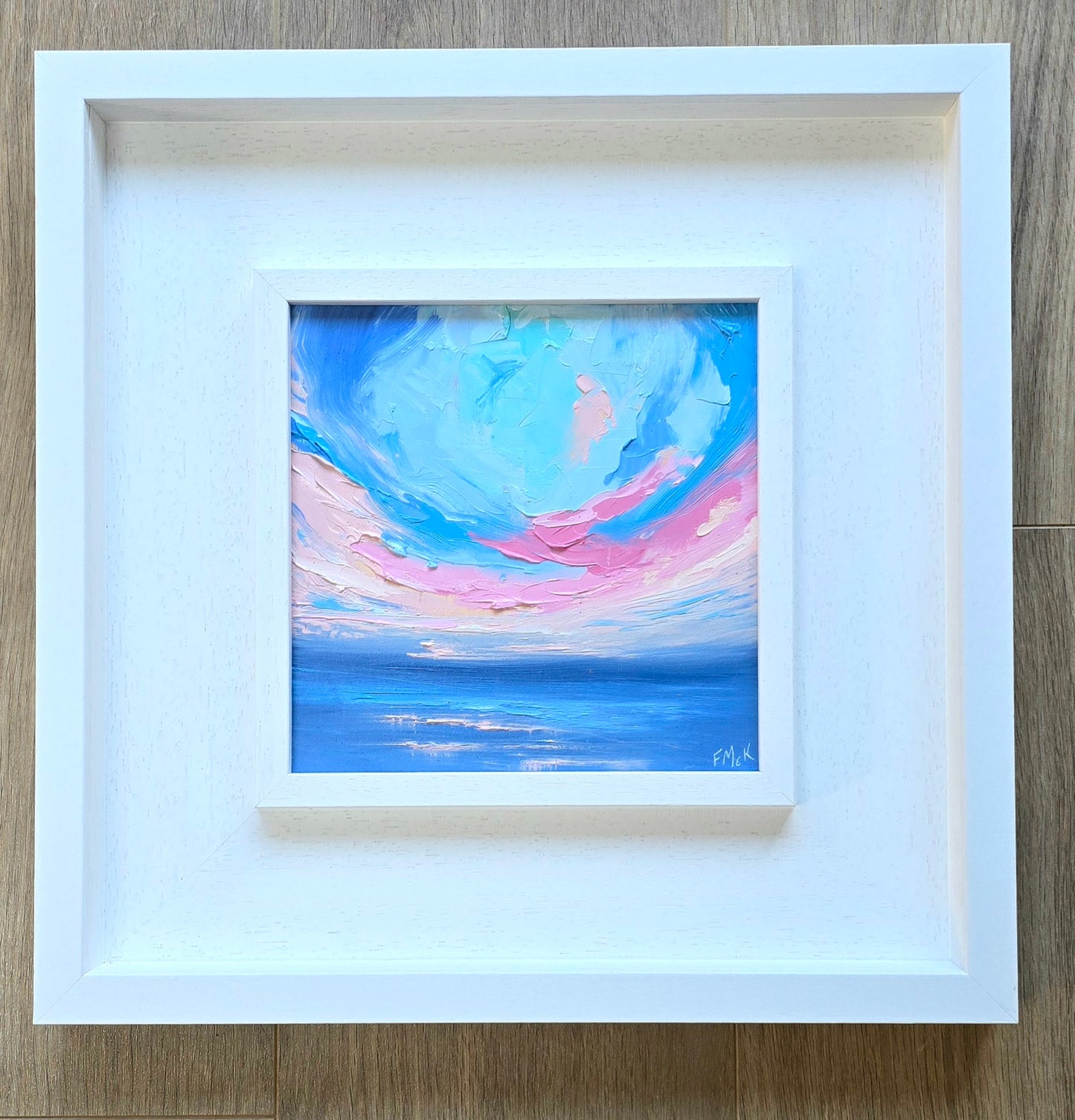 Framed abstract coastal painting with blue and pink hues 