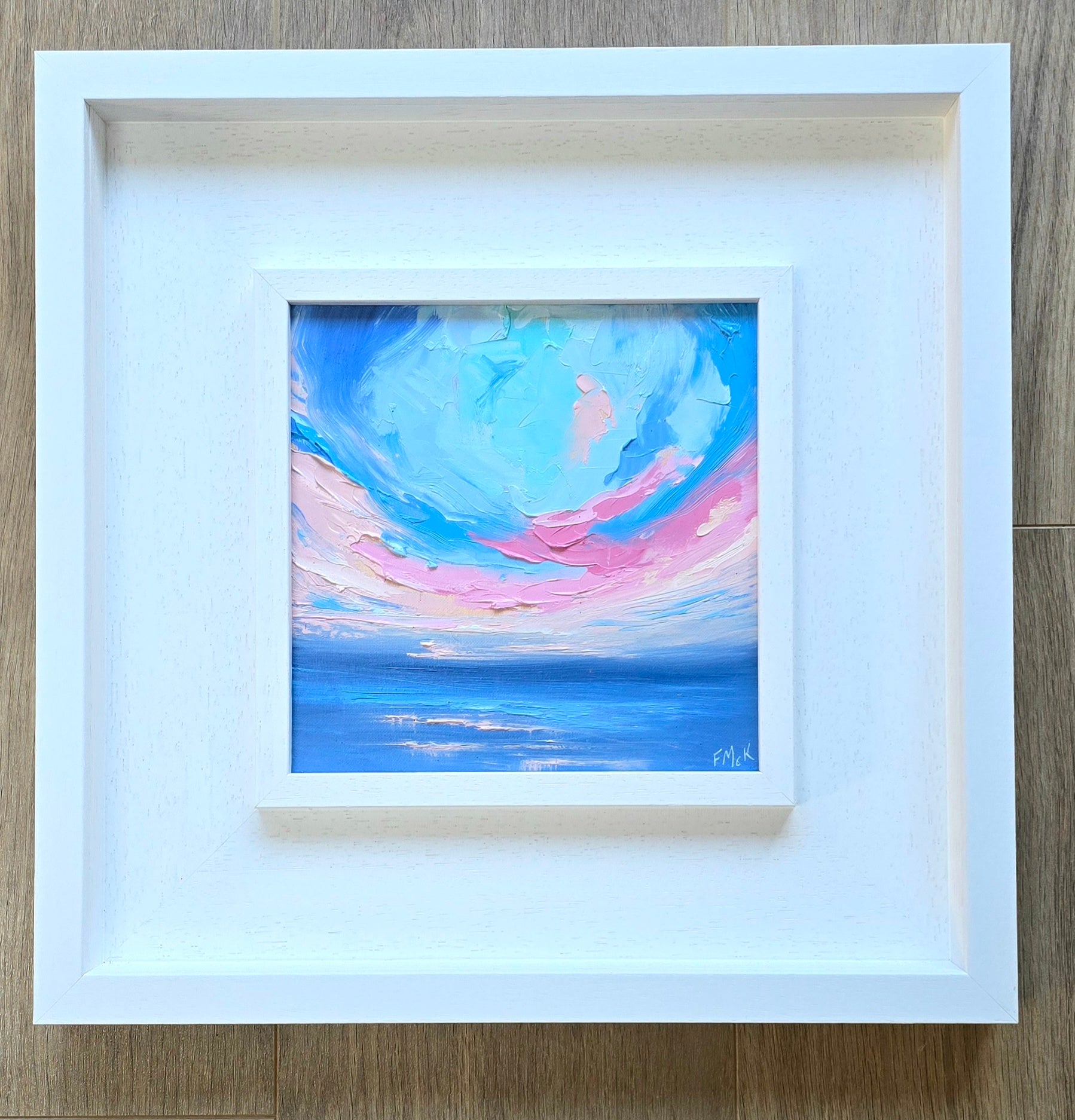 Framed abstract coastal painting with blue and pink hues 