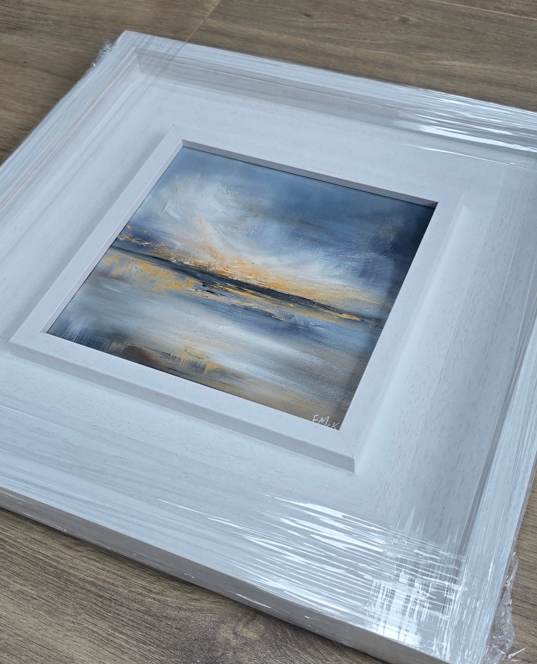 Framed abstract painting with a white frame on a wooden surface