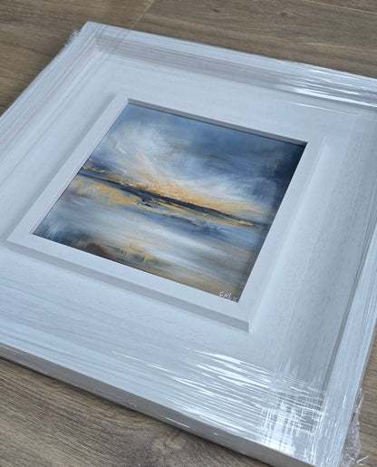 Framed abstract painting with a white frame on a wooden surface