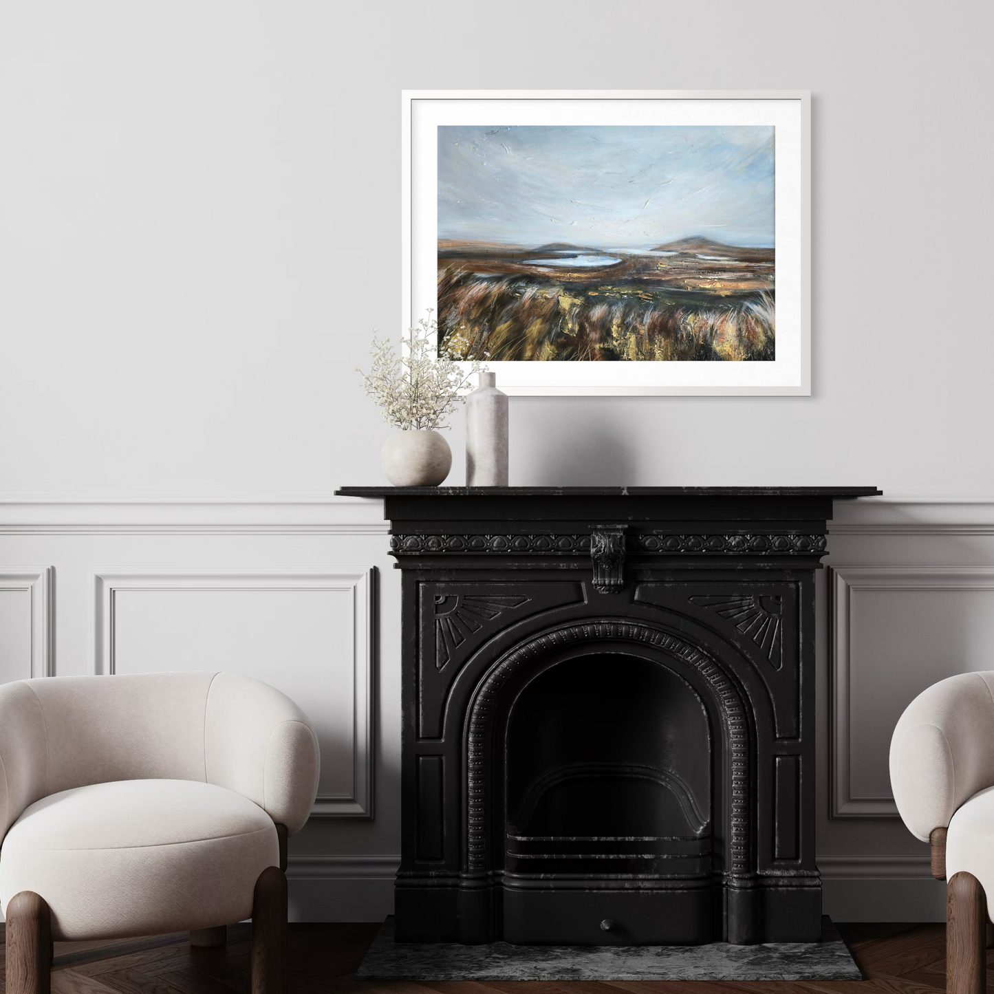 Framed landscape painting above a black fireplace in a room with white walls and beige chairs.