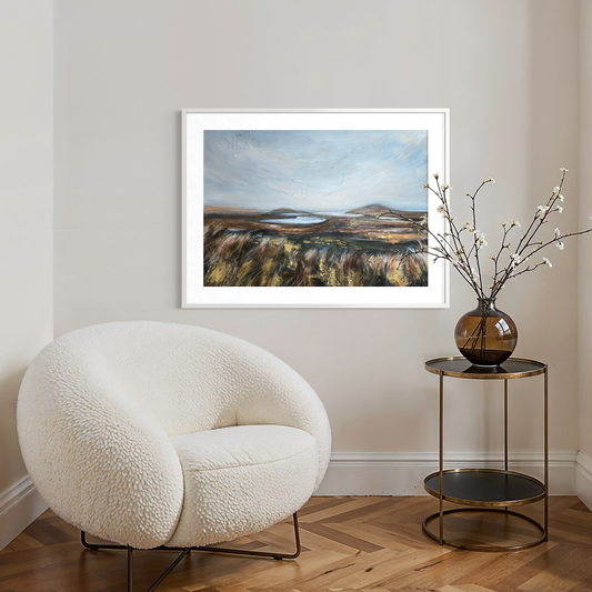 White armchair in a room with a framed landscape painting on the wall and a small table with a vase.