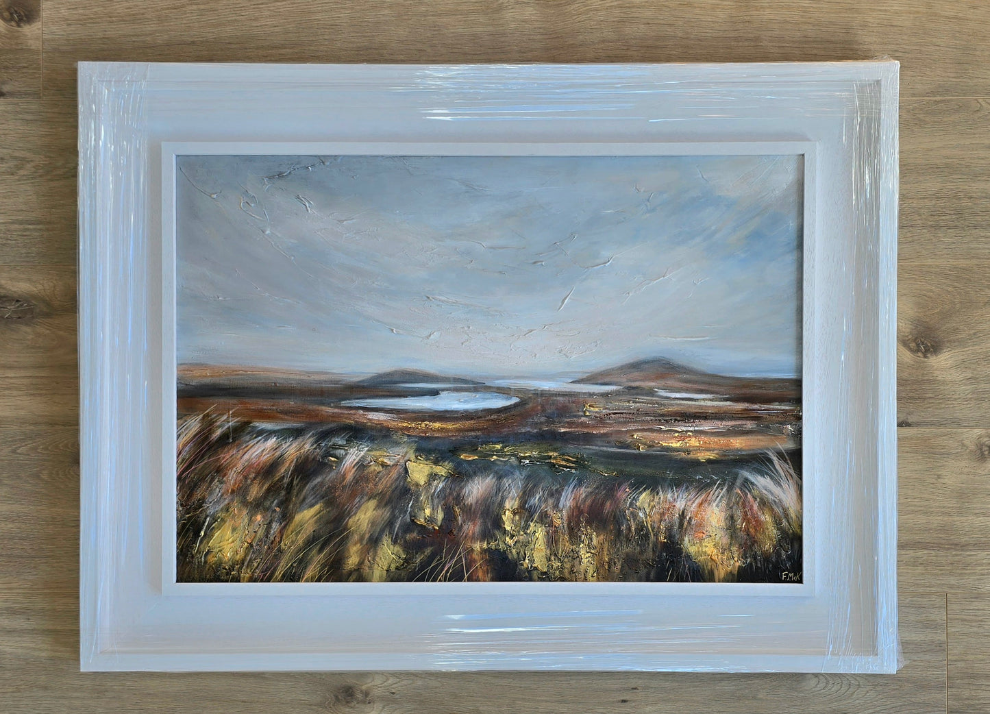 Framed painting of a landscape with a lake on a wooden surface