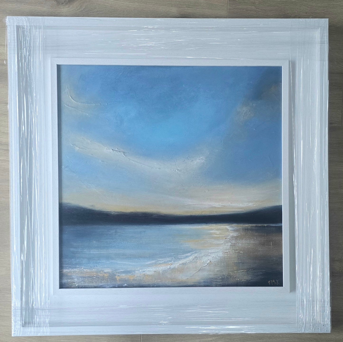 Framed painting of a landscape with a blue sky and water.