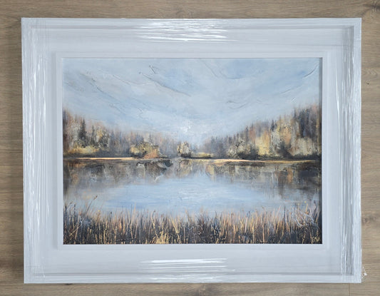 Framed painting of a landscape with a lake and trees on a wooden surface
