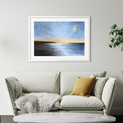 Framed artwork of a sunset over water on a wall above a sofa.