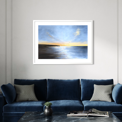 Framed artwork of a sunset over water on a wall above a blue sofa.
