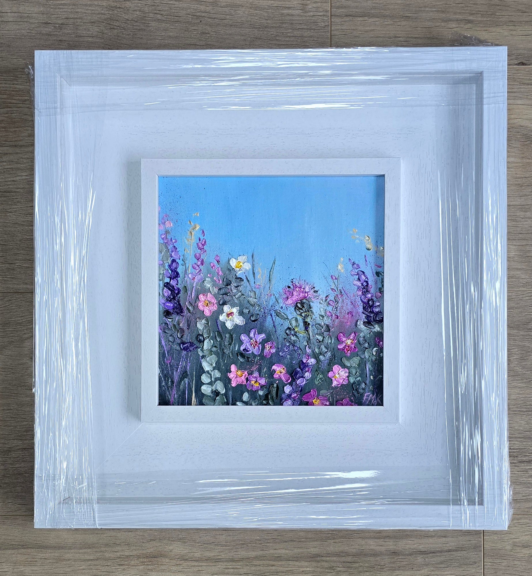 Framed artwork of a colorful floral scene on a wooden surface