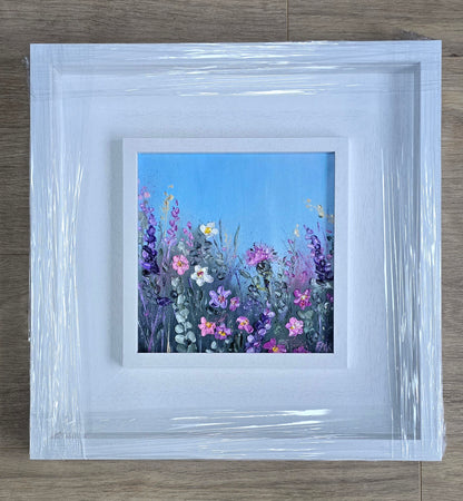 Framed artwork of a colorful floral scene on a wooden surface