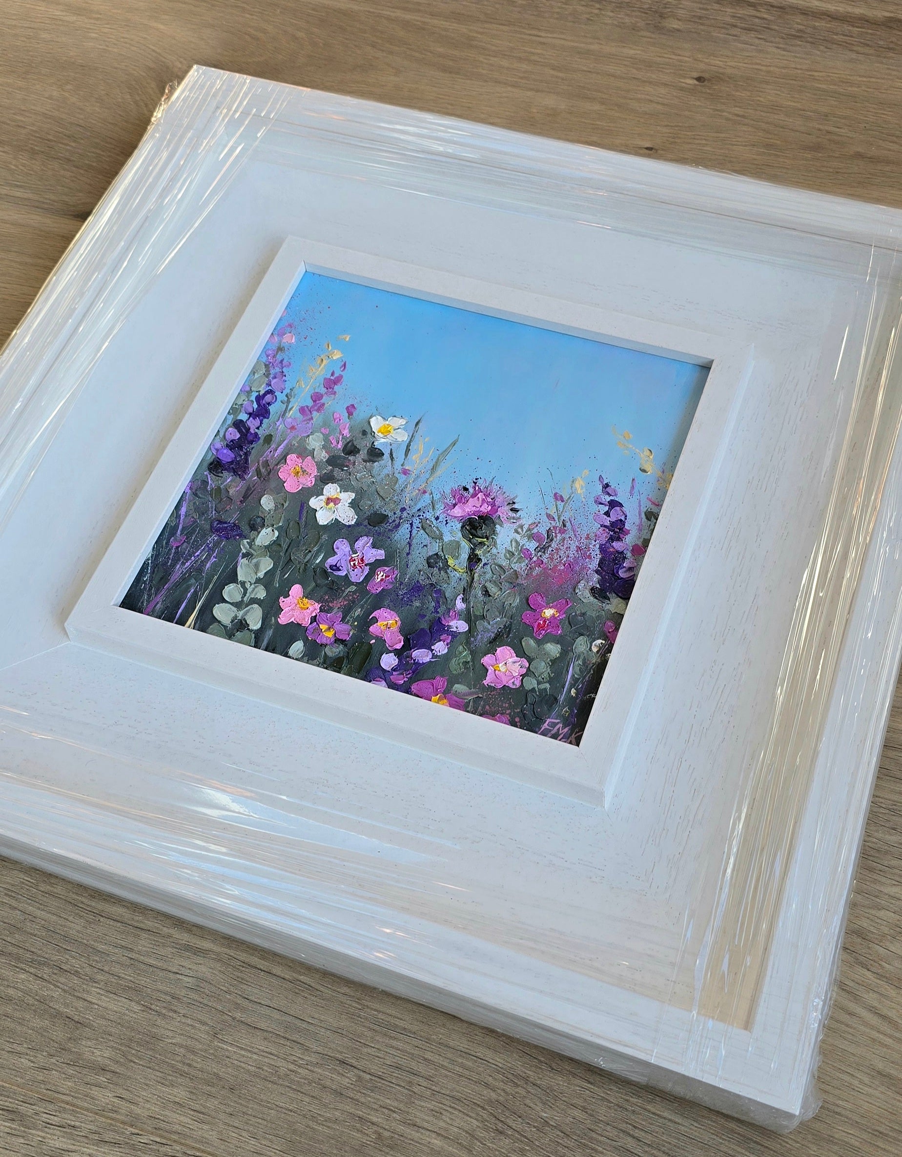Framed painting of wildflowers on a wooden surface