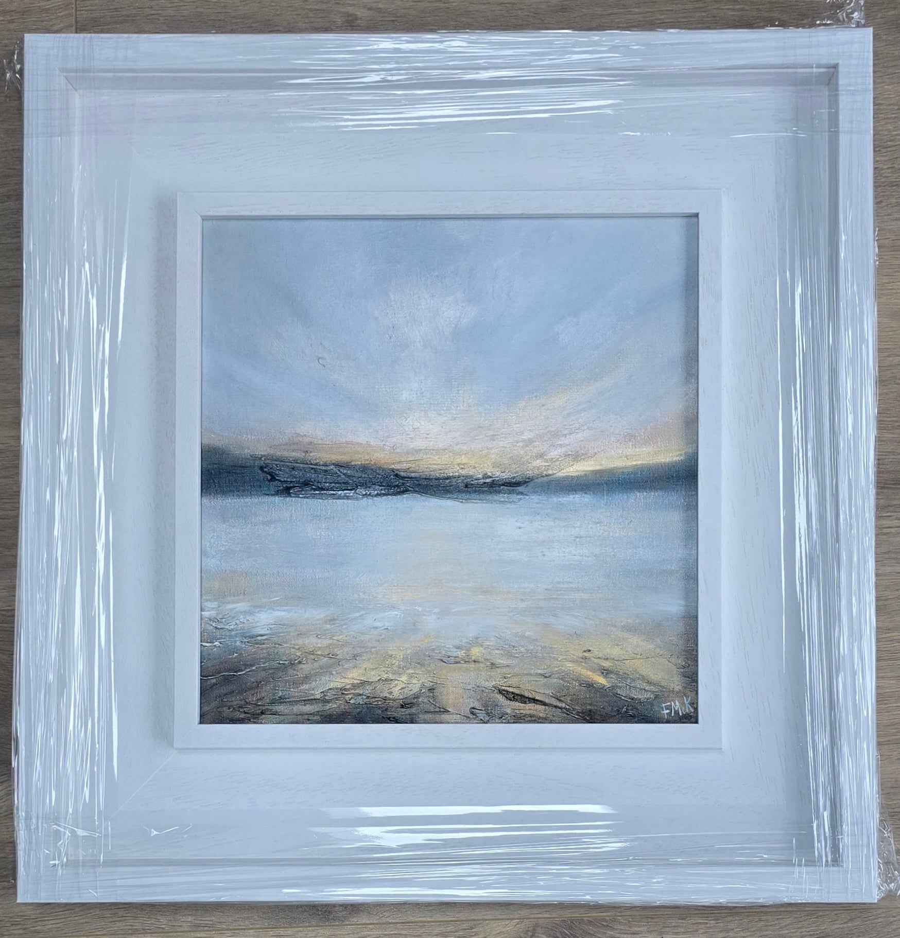 Framed abstract painting with a blue and gray color scheme on a wooden surface