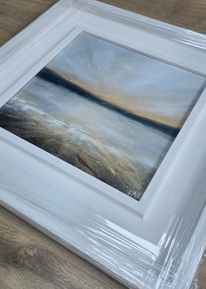 Abstract sunset painting in a white frame on a wooden surface