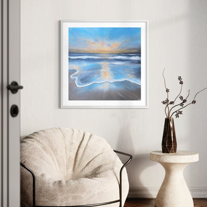 Framed beach painting on a wall above a chair with a vase of flowers on a table.