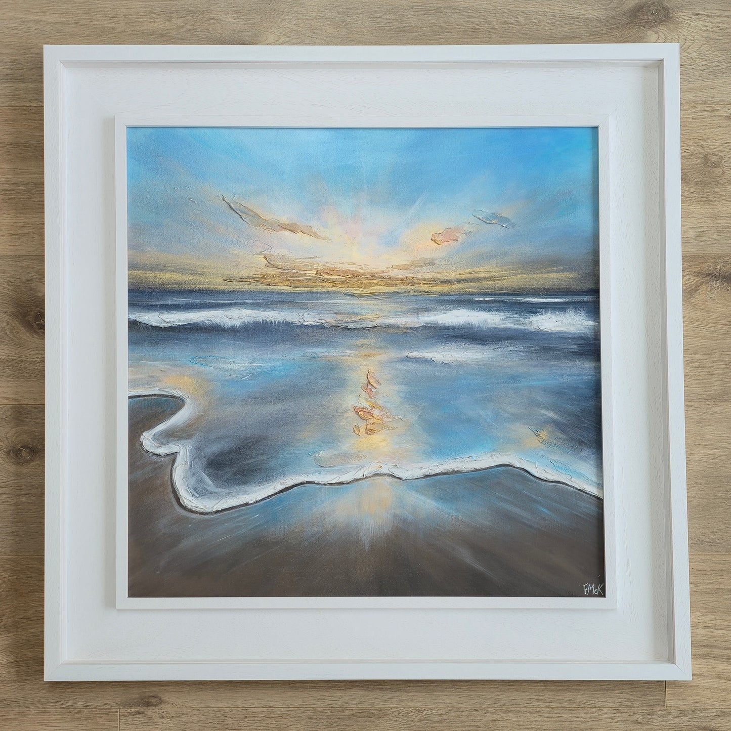 Framed painting of a beach scene with a sunset over the ocean.