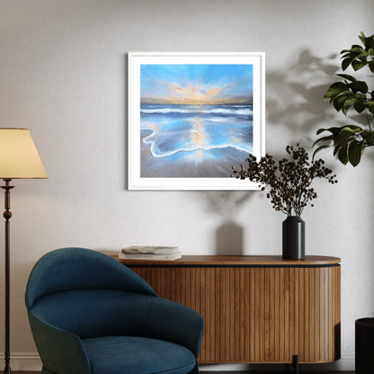 Framed artwork of a beach scene on a wall above a wooden console table with a blue armchair and lamp.