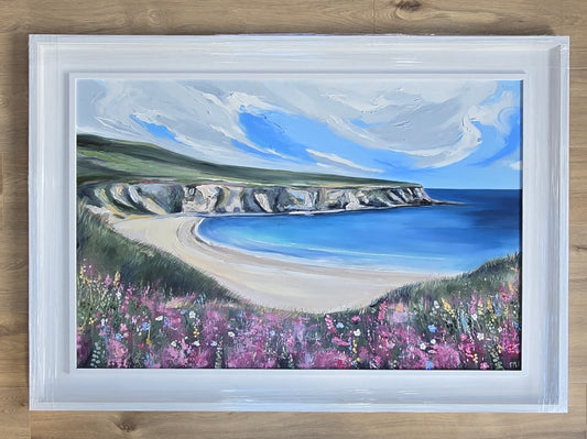 Framed painting of a coastal landscape with a blue sea, cliffs, and pink flowers