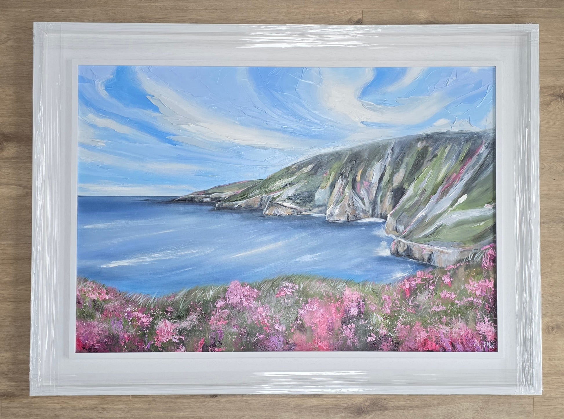 Framed painting of a coastal landscape with flowers on a wooden surface