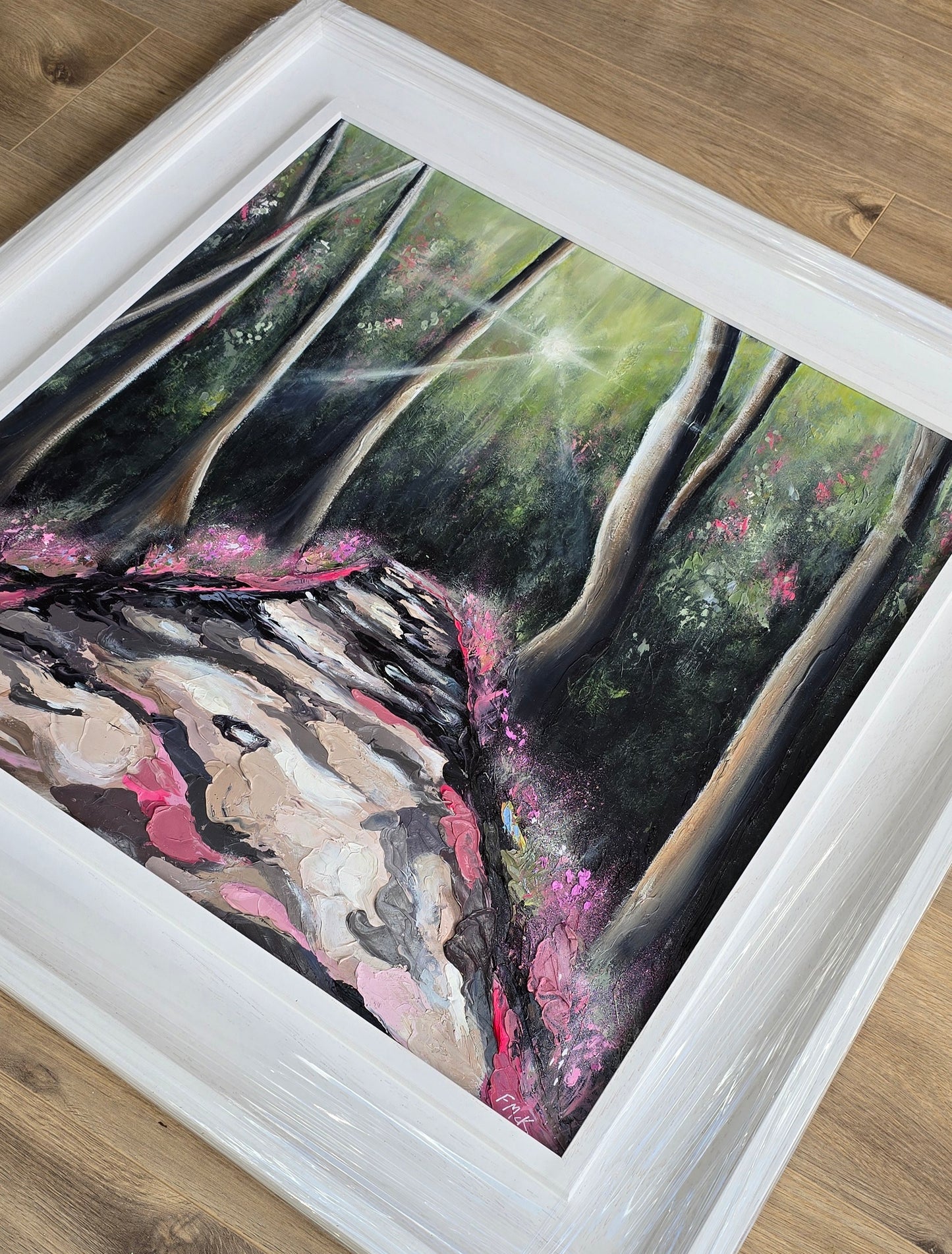 Framed painting of a natural scene with trees and pink flowers