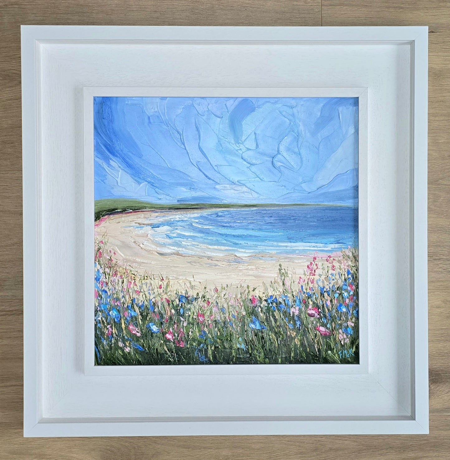 Framed painting of a beach scene with flowers and blue sky.
