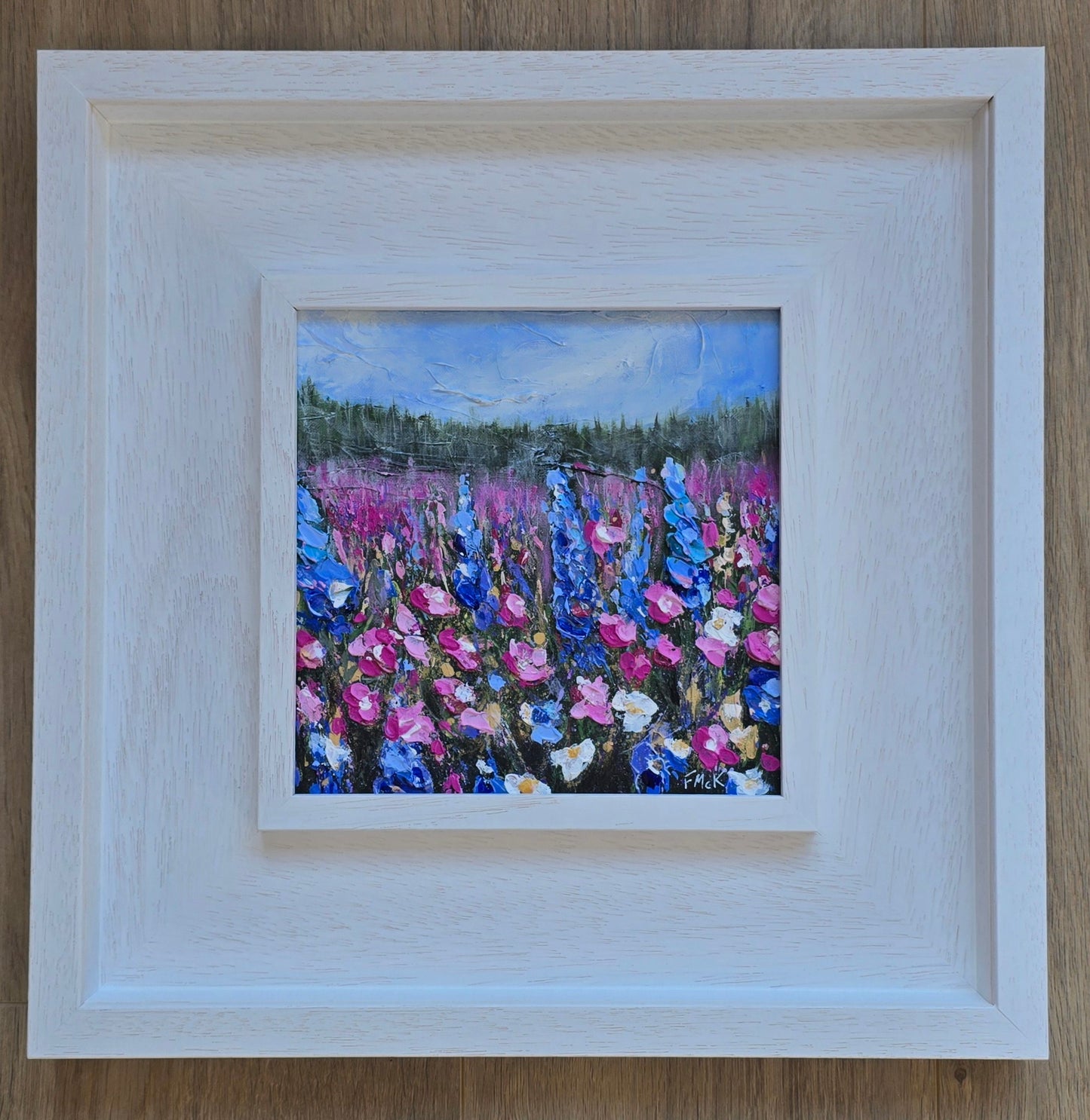 A framed acrylic painting of a field with vibrant flowers, predominantly blue and pink, with a bright sky.