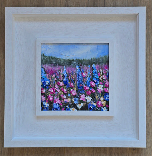 A framed acrylic painting of a field with vibrant flowers, predominantly blue and pink, with a bright sky.