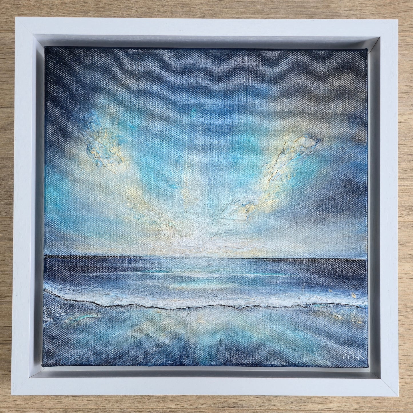 Framed painting of a serene seascape with blue sky and clouds.
