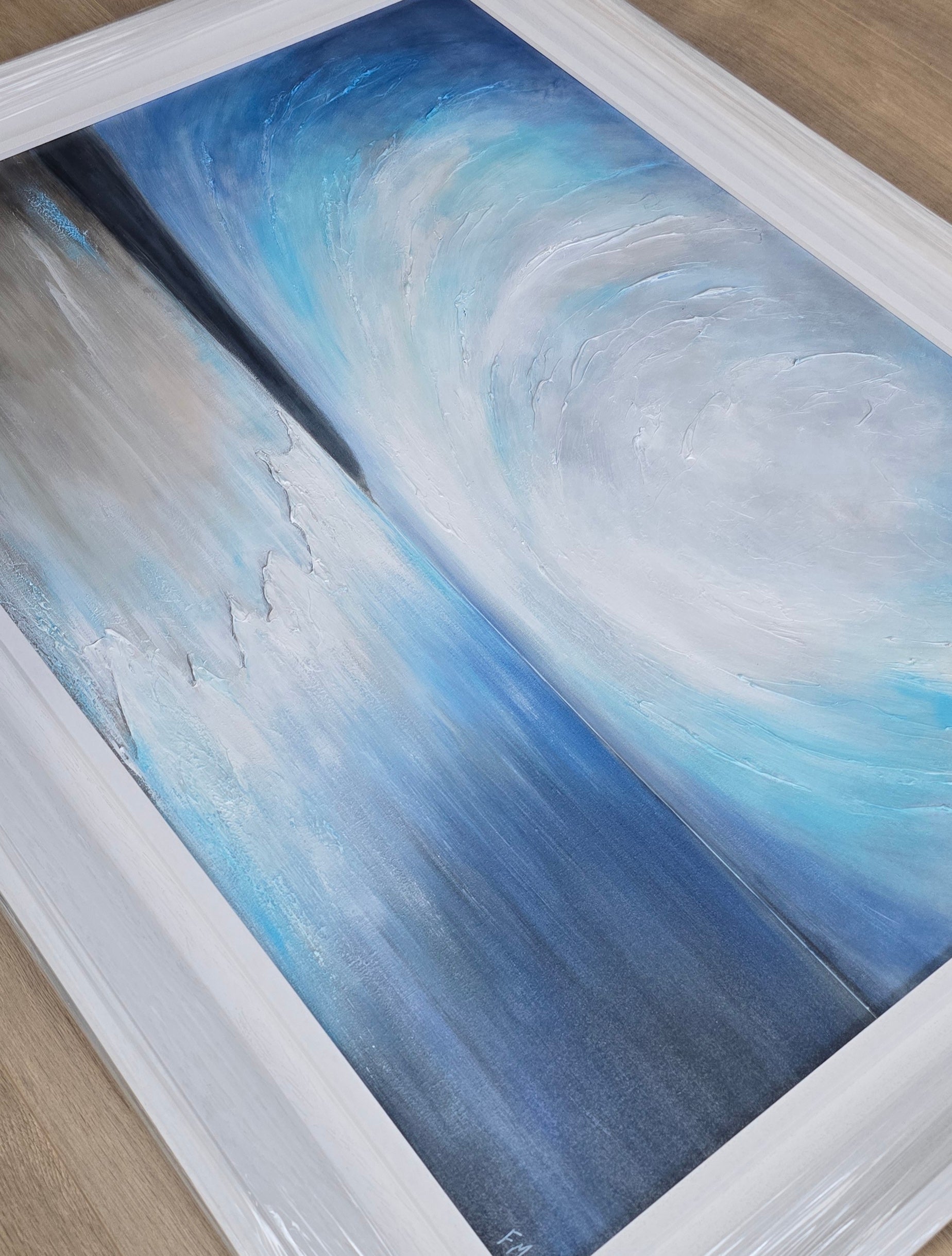 Coastal painting with blue and gray swirls in a white frame.