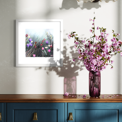 Framed floral print on a wall above a wooden cabinet with a vase of pink flowers.