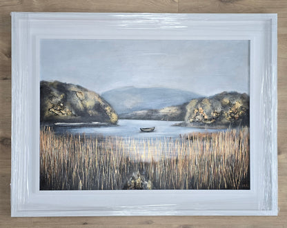 Framed artwork of a landscape with a lake and mountains on a wooden surface
