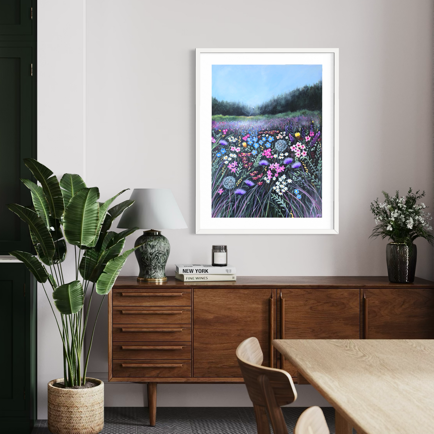 Framed artwork of a floral landscape on a wall above a wooden sideboard.