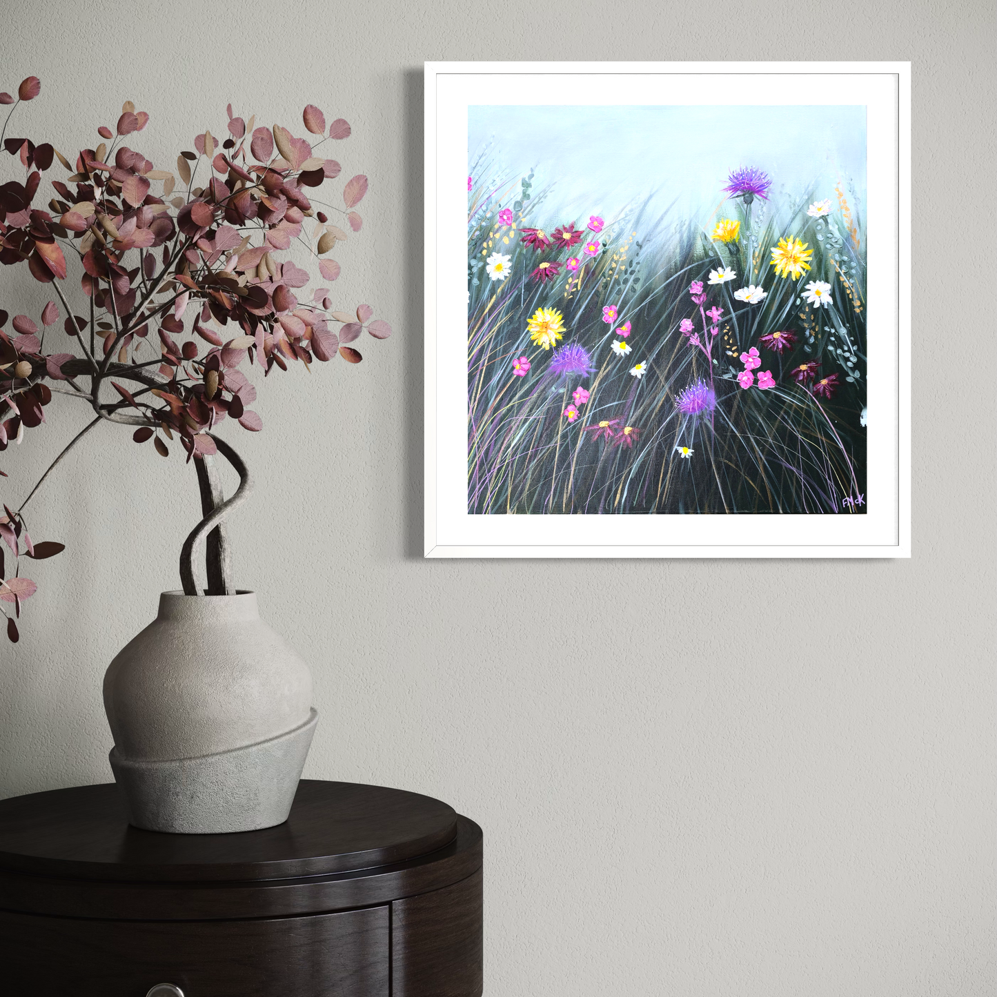 Framed artwork of flowers on a wall above a vase with pink flowers.