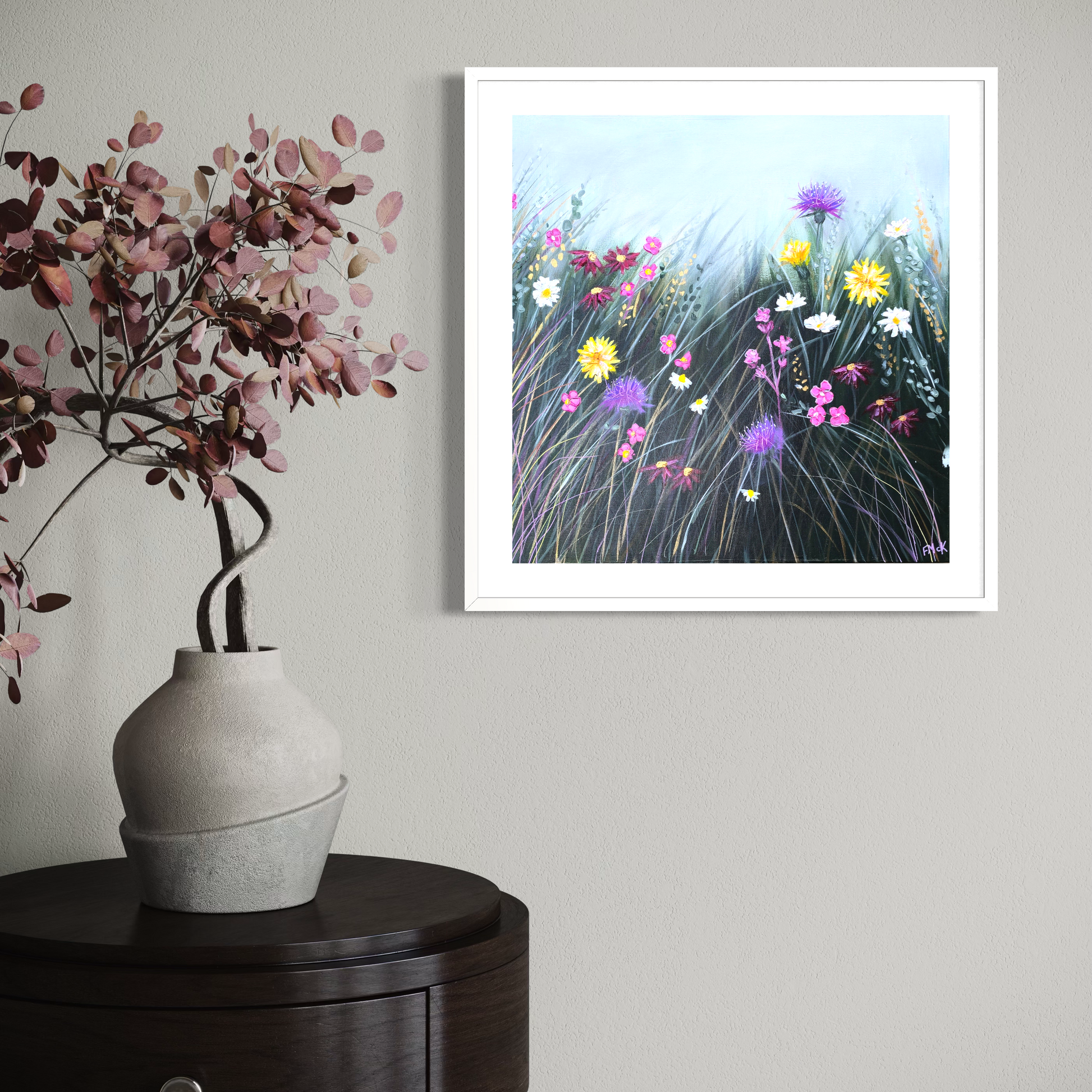 Framed artwork of flowers on a wall above a vase with pink flowers.