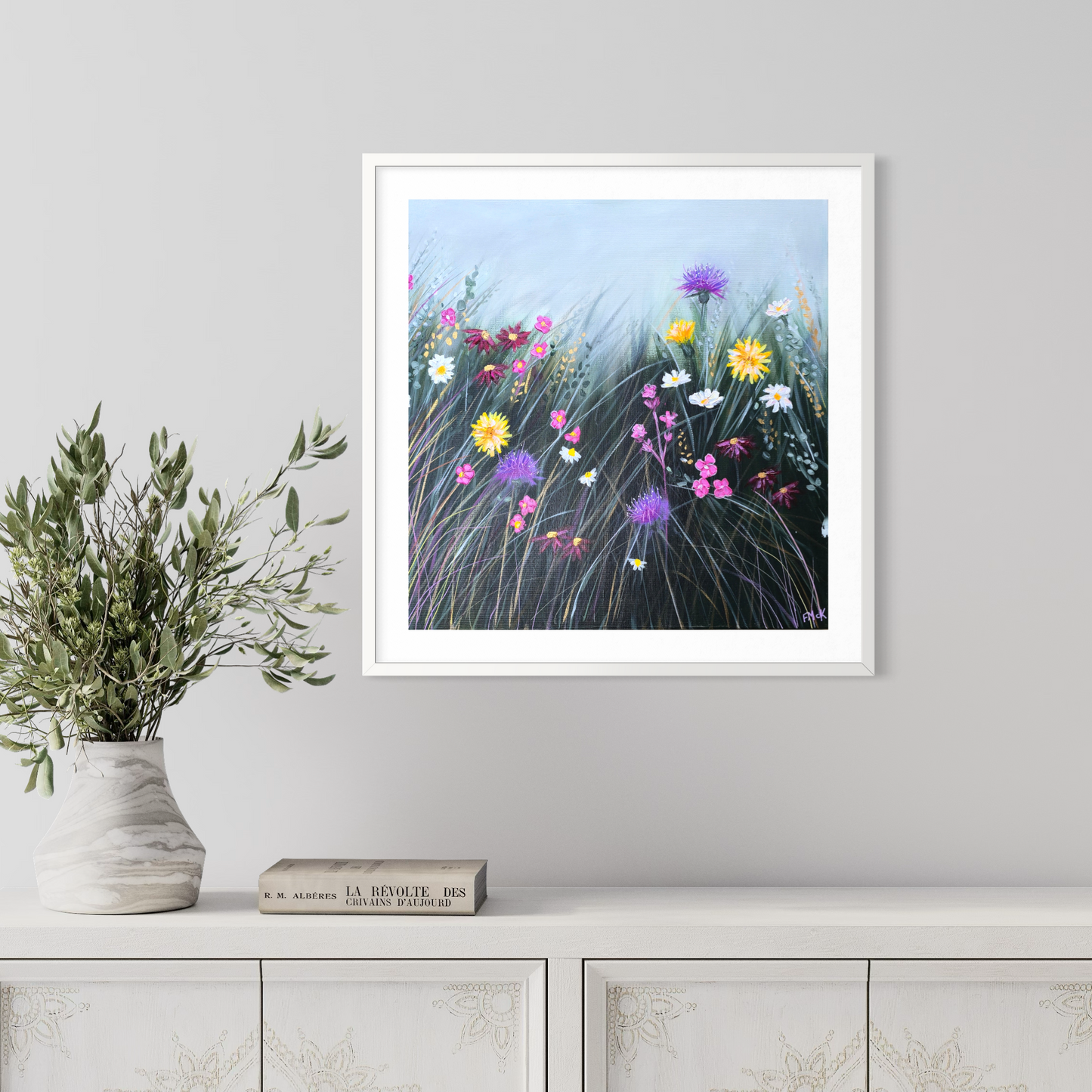 Framed artwork of a colorful floral scene on a wall above a white cabinet.