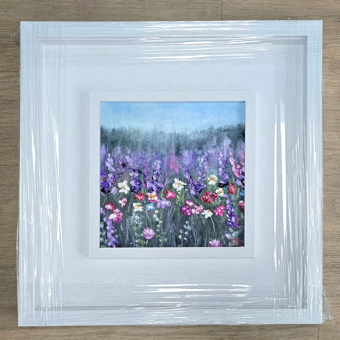 Framed artwork of a floral landscape with a white border on a wooden surface.