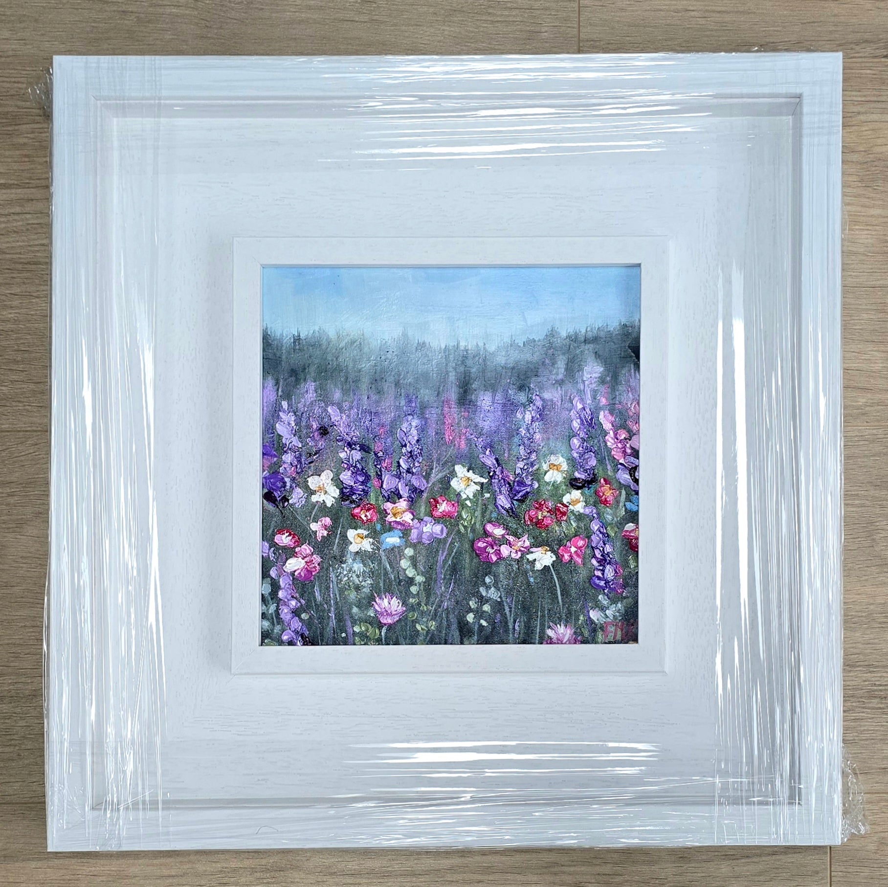 Framed artwork of a floral landscape with a white border on a wooden surface.